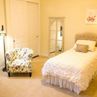 A cozy bedroom featuring a single bed with soft bedding, a floral armchair, and a tall mirror for a minimalist look.