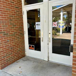 Main entrance with double doors leading into a building, featuring brick walls and informational signage.