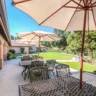 A sunny outdoor patio with tables, chairs, and umbrellas overlooking a lush garden.