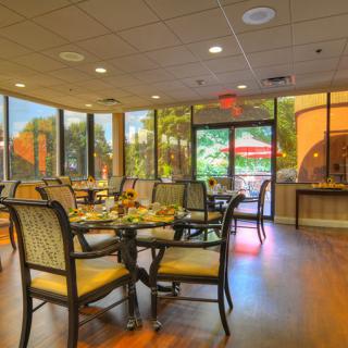 A cozy dining area with tables and chairs, surrounded by large windows letting in natural light.