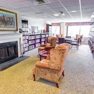 A cozy library space with armchairs, bookshelves, and a fireplace.