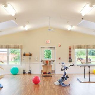 A spacious exercise room equipped with therapy and rehabilitation equipment, including fitness balls, under bright lighting.