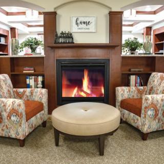 A cozy living room with a fireplace, two patterned chairs, and a round ottoman.