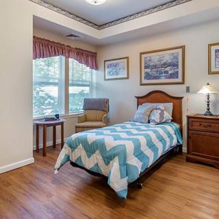 A cozy bedroom with a single bed, chair by the window, and warm lighting.