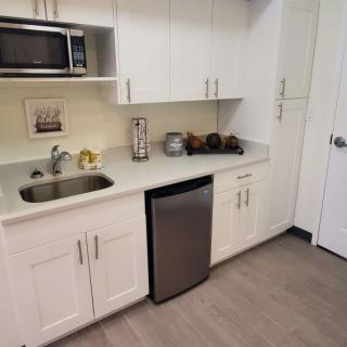A compact kitchen area with white cabinets, a sink, a microwave, and a mini fridge.