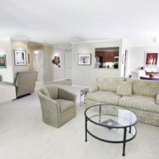 A modern living room with a sofa, chair, and glass coffee table, decorated with artwork.