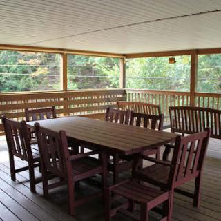 A spacious outdoor dining area with wooden furniture on a covered porch.