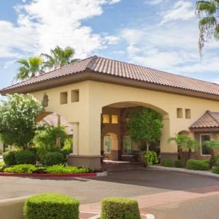 A welcoming entrance to a building with well-maintained landscaping and palm trees under a partly cloudy sky.