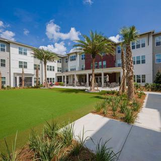 A modern apartment complex with a landscaped courtyard and palm trees on a sunny day.