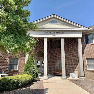 Front view of a brick building with columns and an entrance under a clear blue sky.