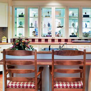 A cozy kitchen interior featuring a wooden counter with two chairs, decorated cabinets, and a window display.