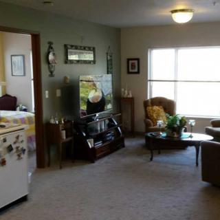 A cozy living room with a television, armchairs, and a coffee table by the window.