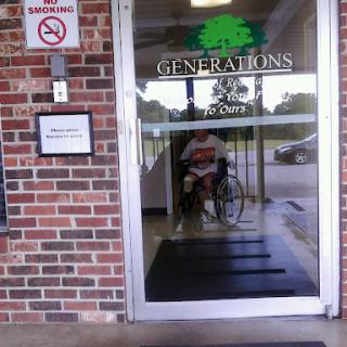 A person sitting in a wheelchair at the entrance of a building named 'Generations'.