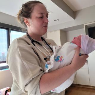A nurse gently holds a newborn baby in a hospital setting.