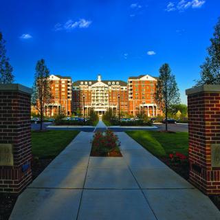A grand brick building framed by a pathway and lush greenery under a clear blue sky.