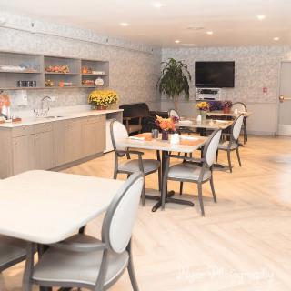 A modern dining area with neatly arranged tables and chairs, featuring a television and decorative plants.
