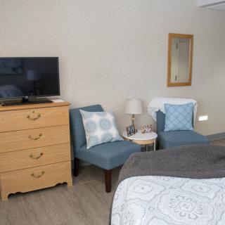 A cozy bedroom with two blue chairs, a wooden dresser, and a TV.