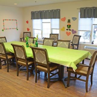 A spacious dining area set up for a gathering, featuring a long table covered with a vibrant green cloth and surrounded by wooden chairs.