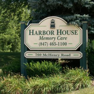 A sign for Harbor House Memory Care surrounded by greenery.