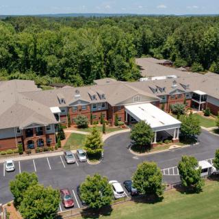 Aerial view of a building complex surrounded by trees with a parking lot and driveway in the foreground.