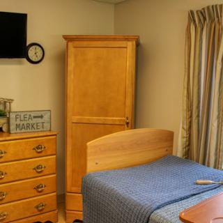 A cozy bedroom featuring wooden furniture, a blue bedspread, and a wall-mounted television.