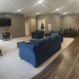 A modern living room with blue sofas, a TV mounted on the wall, and a dining area in the background.