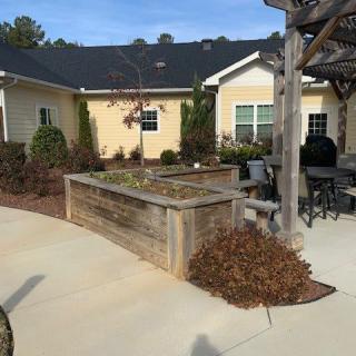 A residential garden patio featuring a wooden planter box, outdoor furniture, and a pergola.