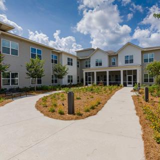 A modern residential building with landscaped pathways and a cloudy sky backdrop.