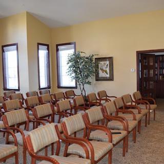 A spacious waiting room featuring several rows of comfortable chairs and natural light from large windows.