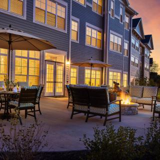 A cozy outdoor patio with comfortable seating and a fire pit, set against an apartment building during sunset.