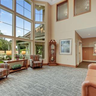 A spacious and bright lobby featuring large windows, comfortable seating, and a decorative clock.