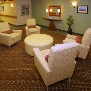 A cozy lounge area featuring a round ottoman surrounded by comfortable chairs with a mirror and plant for decor.