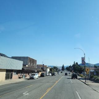 A sunny day in a small town, showcasing the main street lined with shops and vehicles.