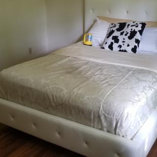 A neatly made bed with a white headboard and cow-print pillow in a simple bedroom setting.