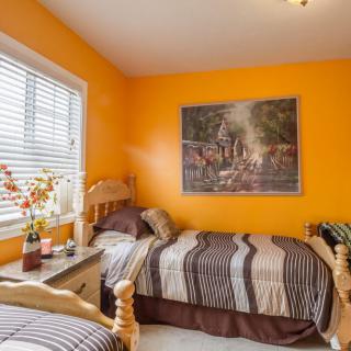 A cozy bedroom with orange walls and twin beds, featuring a window and decorative elements.