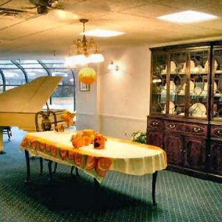 A cozy dining area featuring a grand piano, a decorated table with a yellow tablecloth and floral centerpiece, and an elegant china cabinet in a softly lit room.