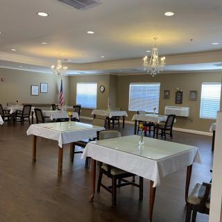A well-lit dining room with neatly arranged tables covered in white tablecloths.