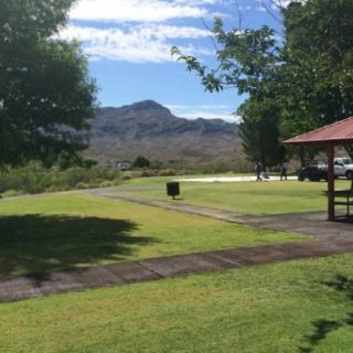 A scenic view of a park with a pavilion, surrounded by lush grass and distant mountains under a clear blue sky.