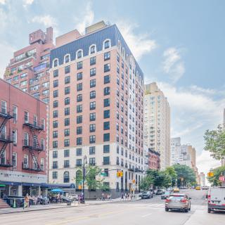 A vibrant city street with tall buildings and light traffic under a clear blue sky.