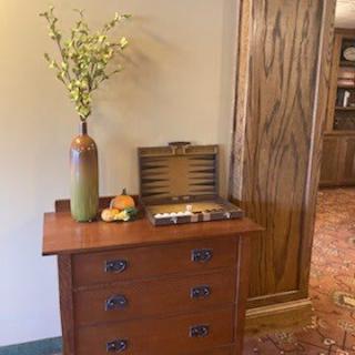 A cozy interior with a wooden chest of drawers adorned with a vase of flowers and a fruit arrangement.
