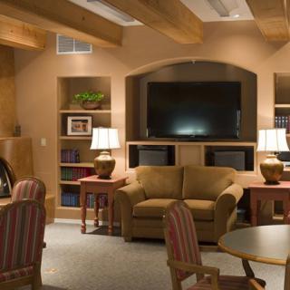 A cozy living room with a sofa and television setup, featuring bookshelves and ambient lighting.