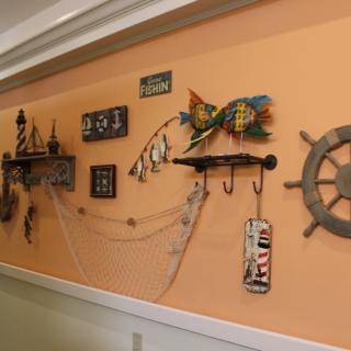 A wall adorned with nautical-themed decor, including a ship wheel, colorful fish, anchors, seashells, and a decorative fishnet.