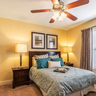 A cozy bedroom featuring elegant decor with a ceiling fan, framed artwork, and ambient lighting from bedside lamps.