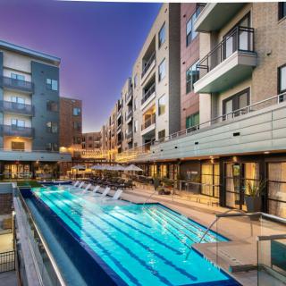 A modern apartment complex featuring an illuminated outdoor pool at dusk.