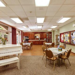 A cozy dining area with a piano, tables, and chairs adjacent to a kitchen.