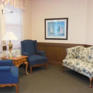 A cozy living room with blue armchairs, a floral-patterned couch, and a framed painting on the wall.