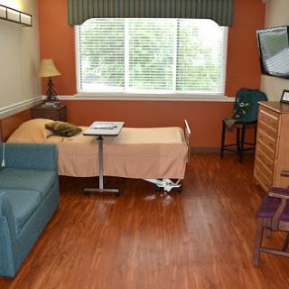 A well-furnished hospital room featuring a patient bed, a sofa, and natural light from the window.