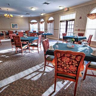 A spacious dining room with elegantly set tables and chairs, bathed in sunlight streaming through large windows.