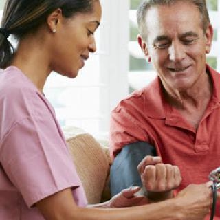 A nurse taking the blood pressure of an elderly patient in a comfortable home setting.