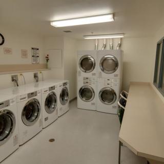 A commercial laundry room with washing machines and dryers lined up against the walls.